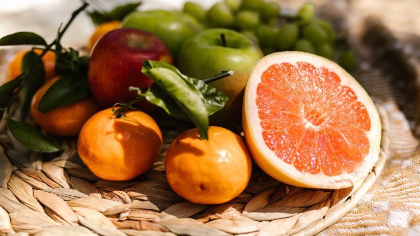 Vibrant assortment of fresh fruit including citrus and apples placed in a natural setting.